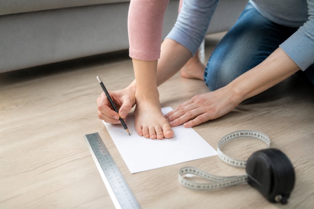 Parent tracing a child's foot on paper to measure kids feet accurately at home