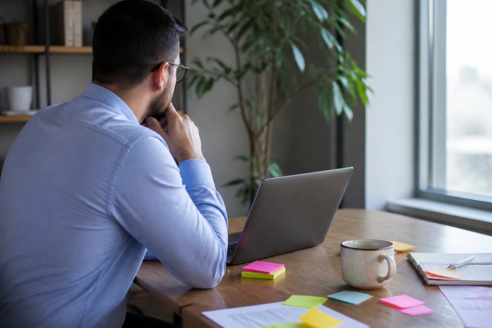 A business analyst reviewing mobile app performance dashboards on a laptop in a modern office, sticky notes on the desk beside a half-finished coffee, soft daylight from a window