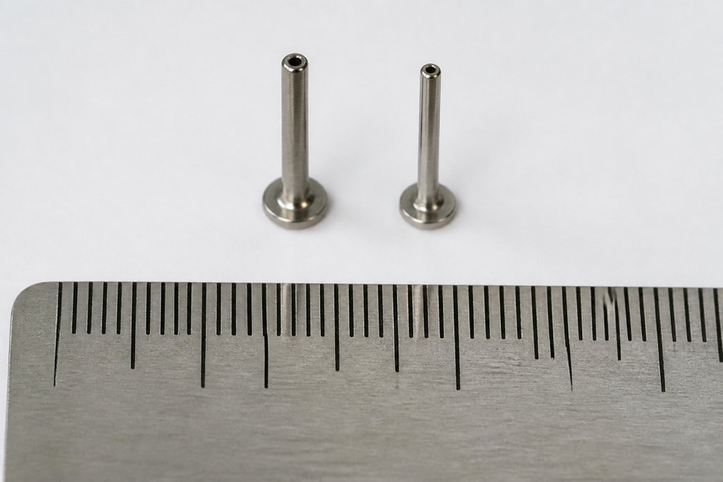 Macro comparison of 16g and 18g titanium labret posts with a millimeter ruler for accurate piercing size scale