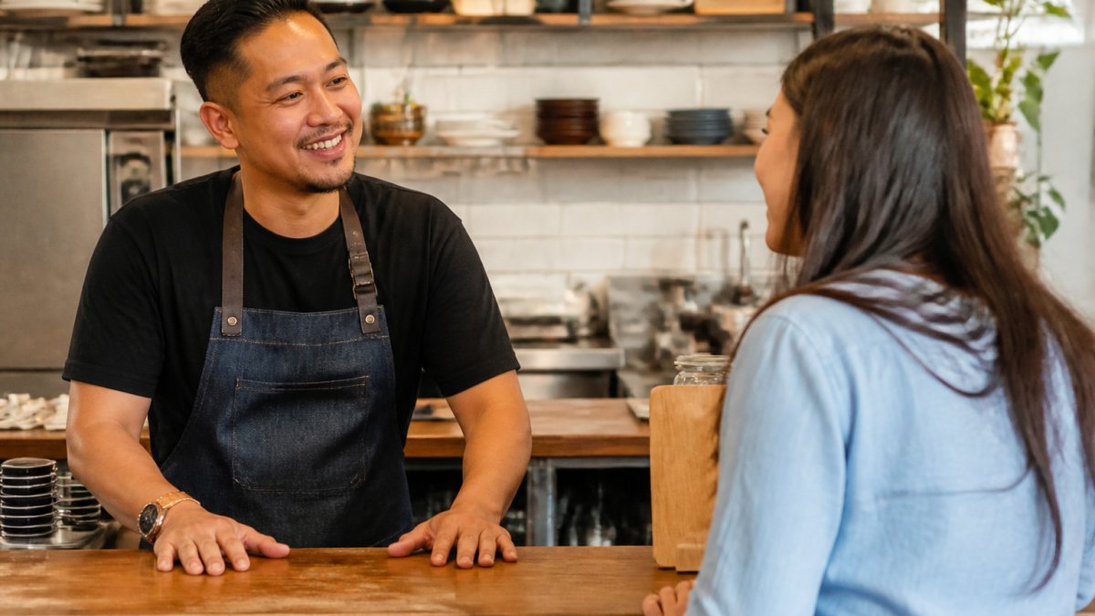 Restaurant manager or owner smiling while speaking with a regular customer at the counter, showing friendly conversation and community connection