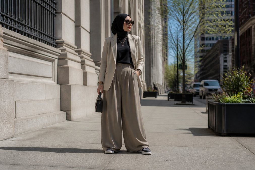 A confident woman in modest streetwear, a structured blazer over a relaxed wide-leg trouser, standing in a bright urban setting with natural daylight, styled for both professional and casual wear