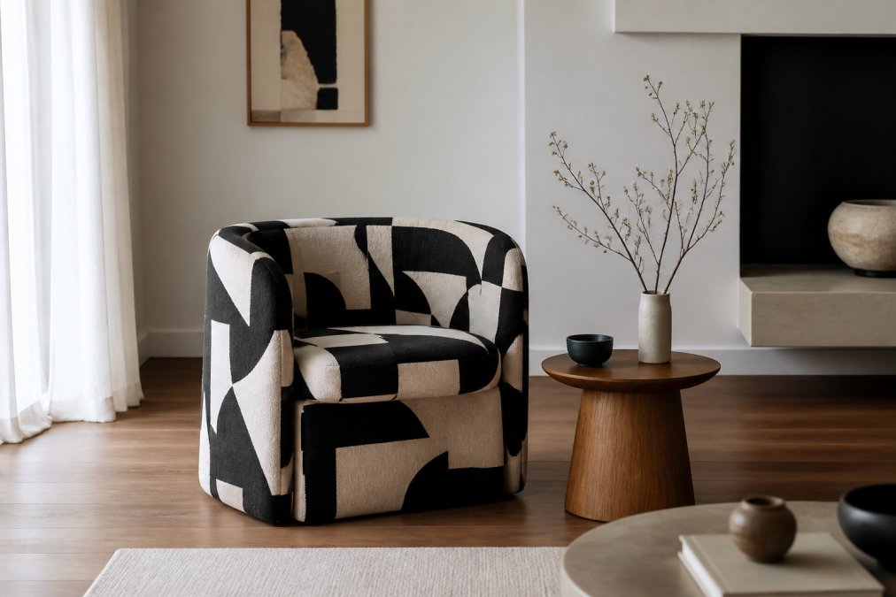 A sculptural statement chair with geometric upholstery positioned in a minimalist living room with soft neutral walls, warm wood flooring, and a simple wooden side table, demonstrating how a bold piece anchors a calm space