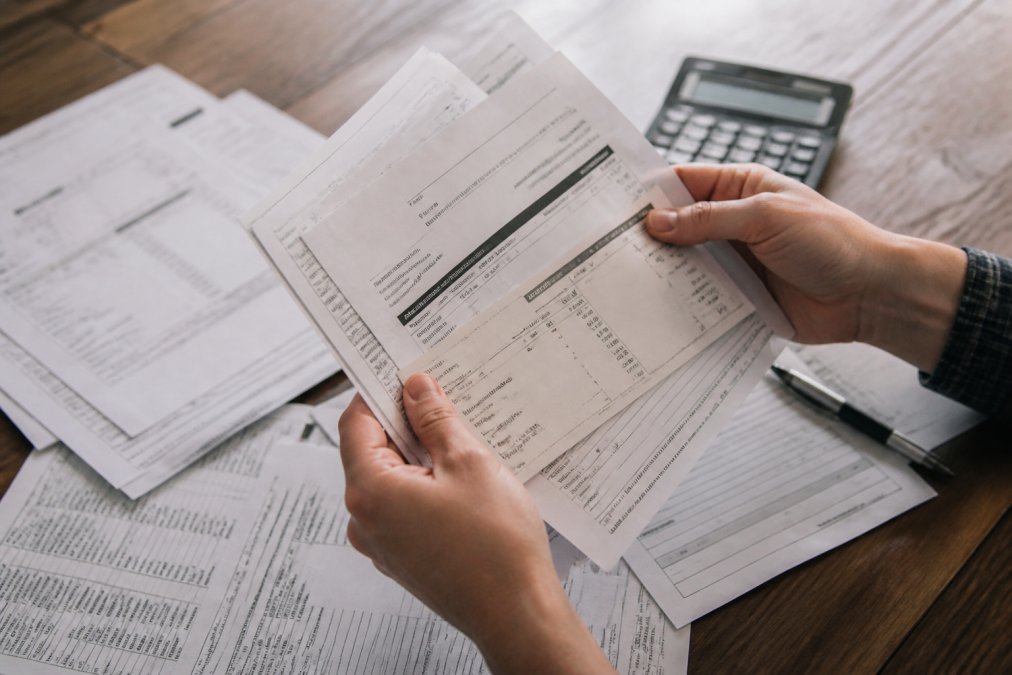 Close-up of hands holding financial documents and pay stubs on a desk with a calculator and pen nearby