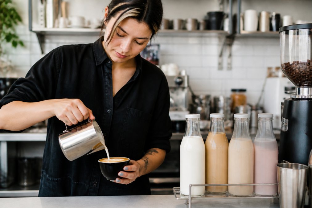 Barista pouring steamed oat milk into an espresso cup to help you order vegan coffee in a modern cafe