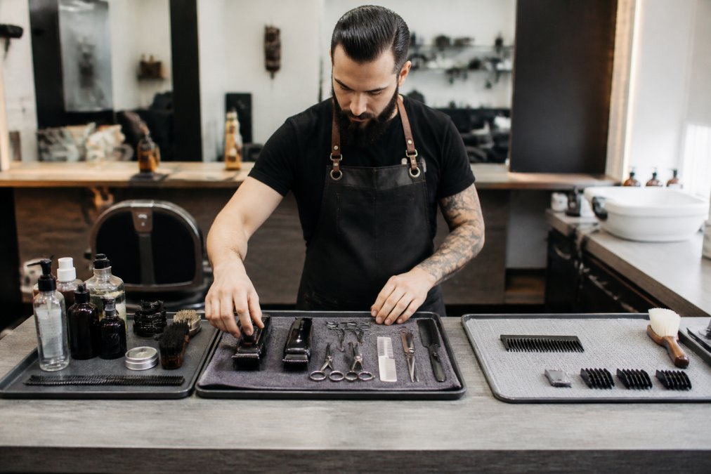 A professional barber working at a clean station with clippers, shears, and combs arranged in distinct prep, service, and cleanup zones on the counter