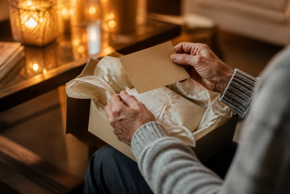 A close-up of a parent's hands unwrapping a gift box with a personalized note card, surrounded by warm ambient lighting