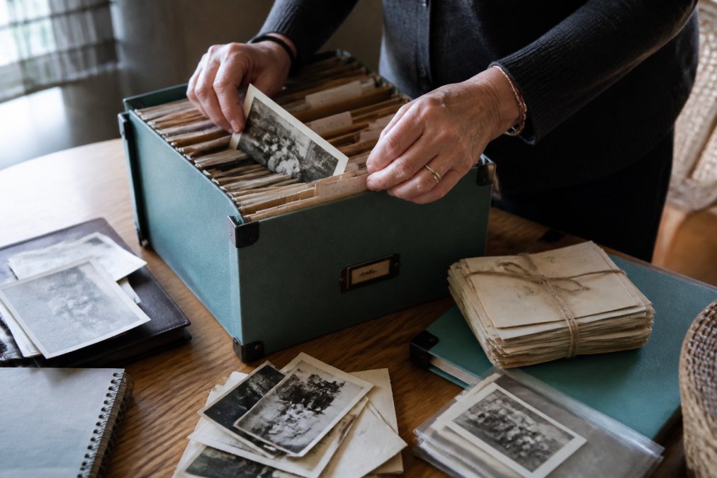Close-up of hands carefully arranging old family photographs, letters, and documents in an organized filing system or memory box