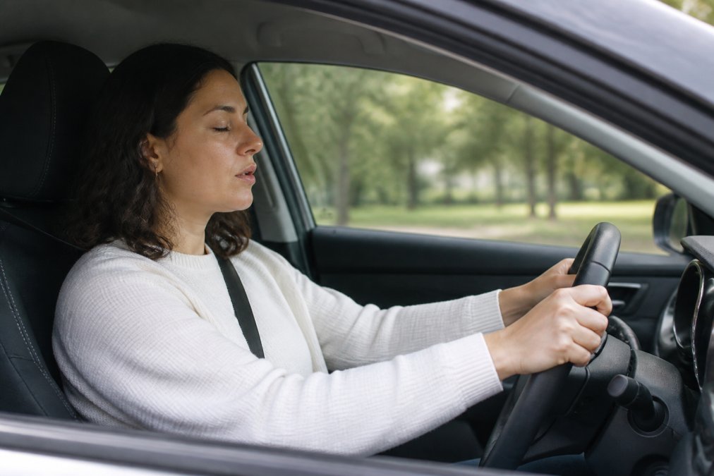 Person sitting in the driver's seat of a parked car with hands on the steering wheel, practicing deep breathing with a calm, focused expression