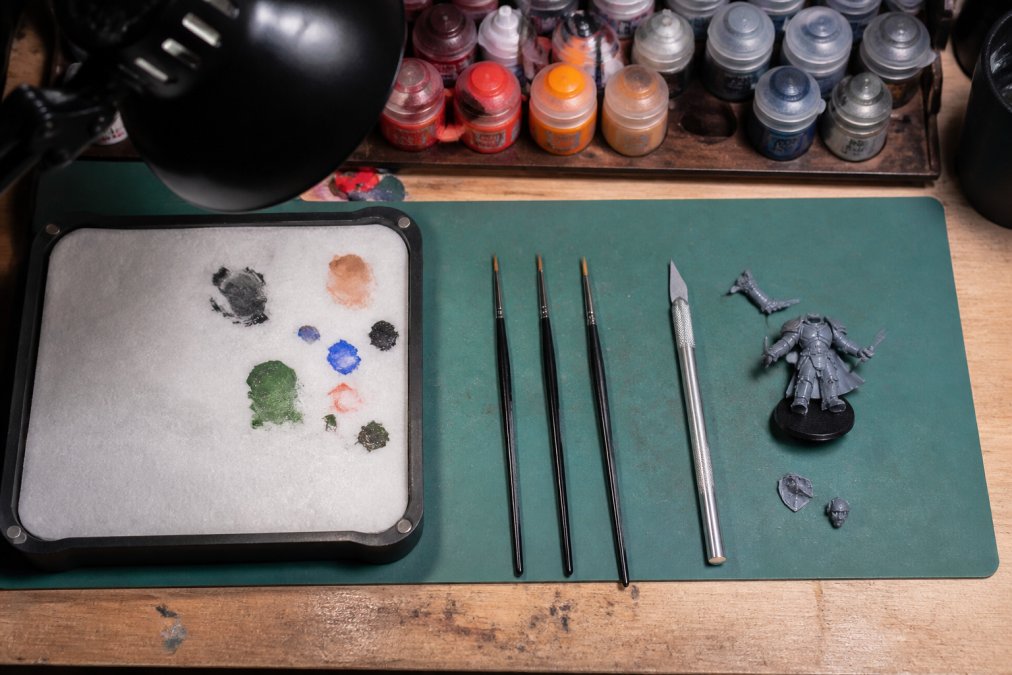 Hobby desk with a wet palette, brushes, and tools to learn how to paint unpainted gaming miniatures.