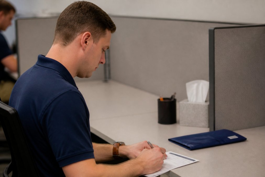 Professional test-taker seated at computer workstation in quiet testing center, focused on screen, with testing monitor visible and neutral office lighting
