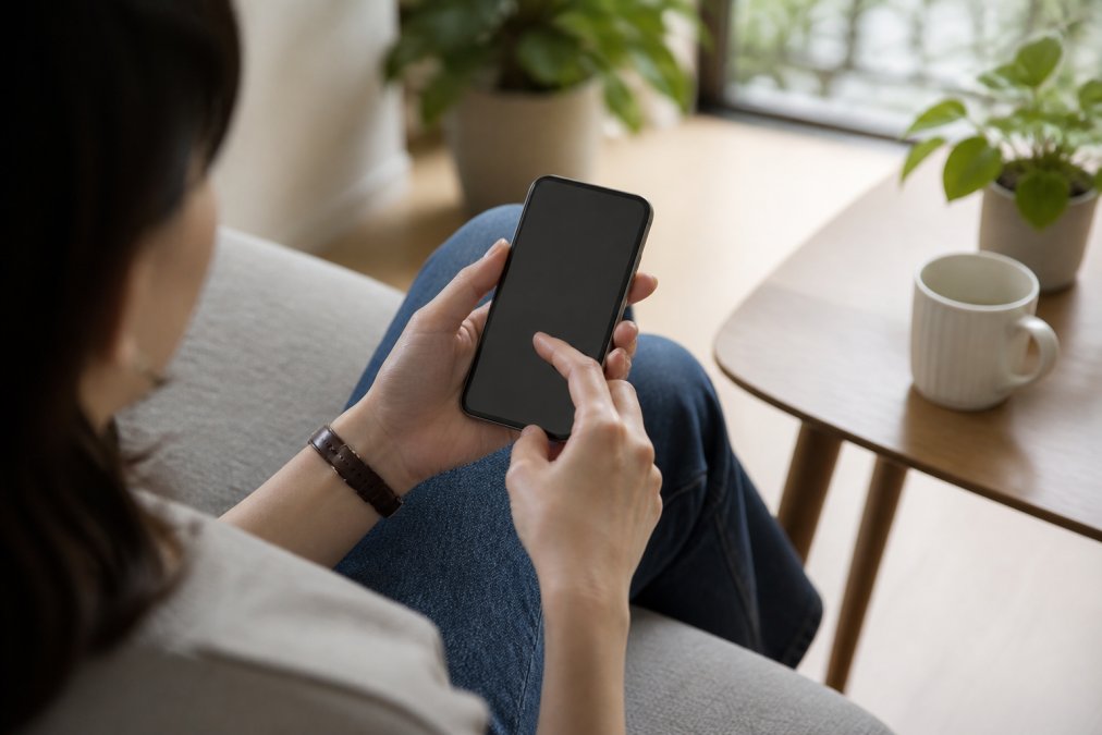 Close-up of smartphone in hands displaying mobile subscription app interface with pause delivery option visible on screen, natural daylight
