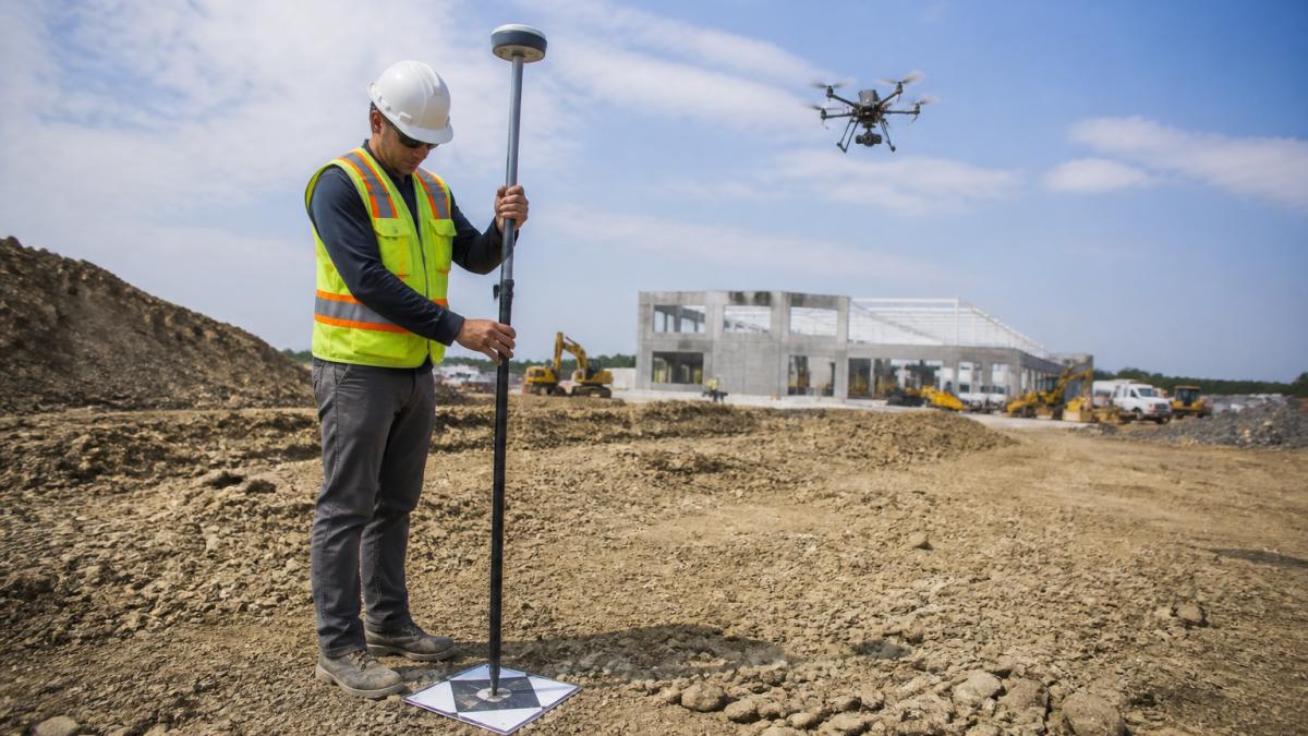 Surveyor using an RTK GPS receiver on a ground control point for drone photogrammetry on a construction site
