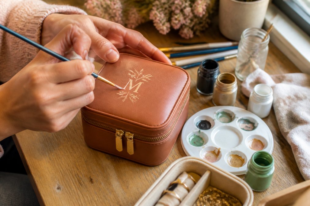 Hands hand-painting initials on a leather jewelry box to show how to personalize a gift without engraving.