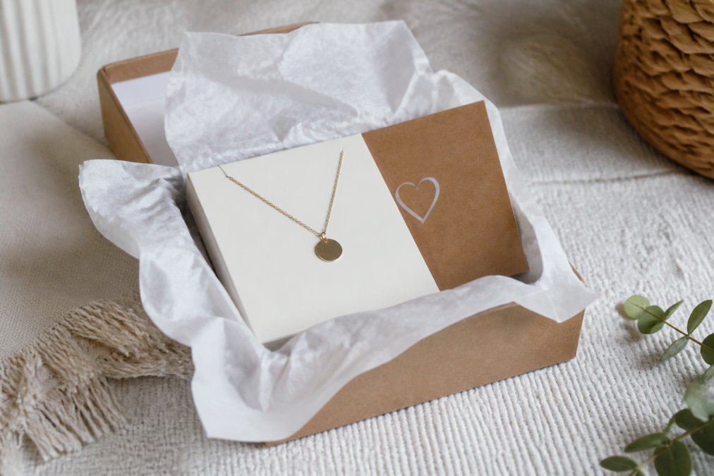 A personalized necklace or bracelet displayed on a minimalist gift box with tissue paper and a handwritten note card, photographed in natural light