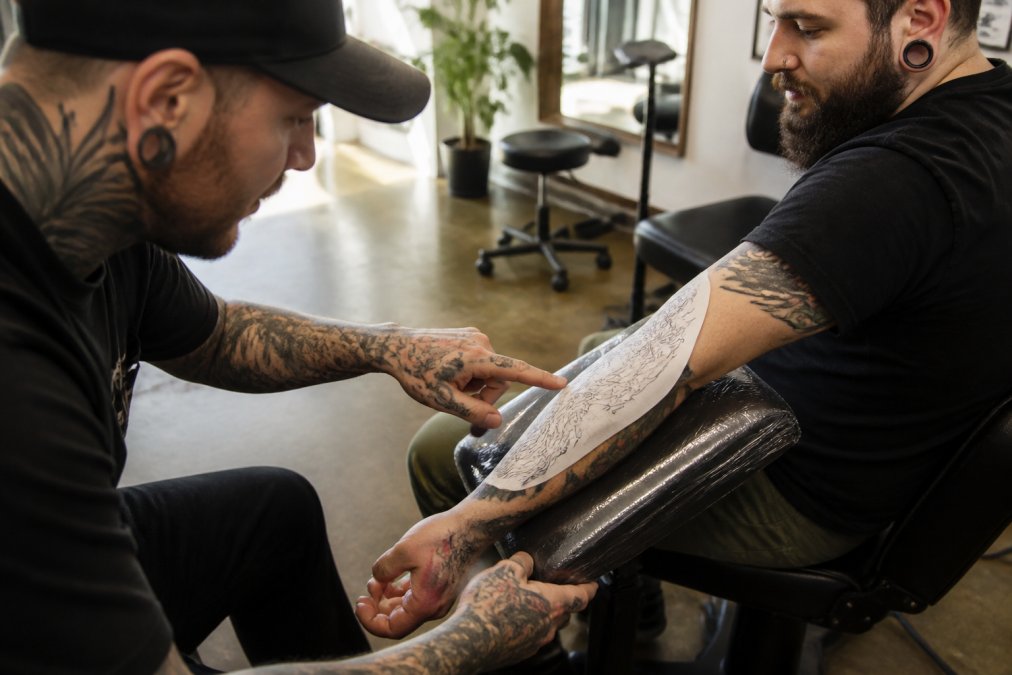 Tattoo artist and client reviewing stencil placement on a forearm to ensure the design flows with the muscle.
