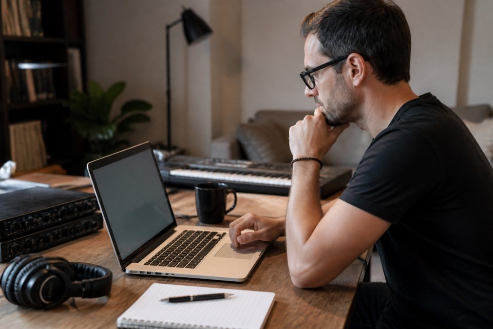 Professional musician or producer at desk with laptop, reviewing an email draft on screen with headphones and notebook nearby, focused on crafting a professional pitch