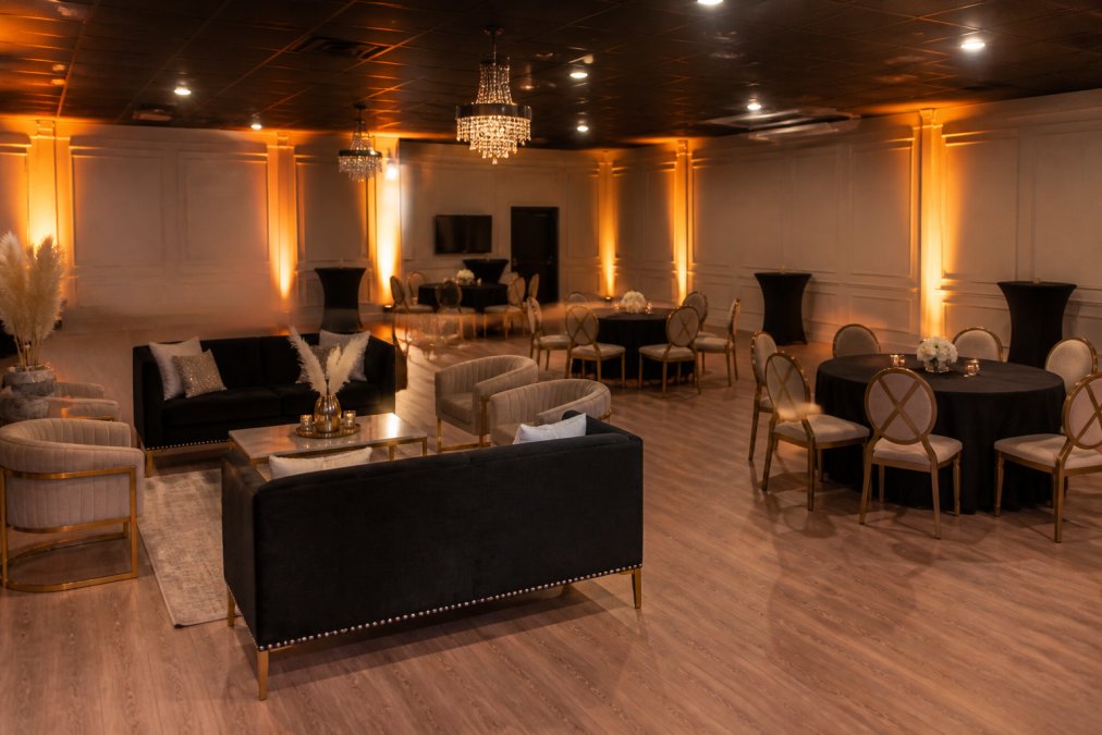 A sophisticated event space set up for a corporate retreat, with plush lounge furniture arranged in conversation clusters, warm amber up-lighting along the walls, and round tables for small groups of six, photographed from a wide angle in a warmly lit interior