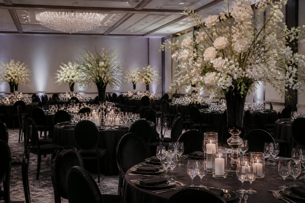 An elegant wedding reception setup with monochrome decor, lush floral installations, and soft up-lighting in a sophisticated venue