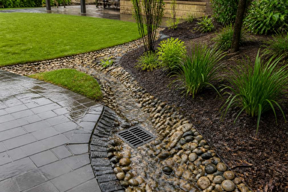 Landscaped garden showing visible drainage channels with gravel swales and permeable paving, demonstrating how water flows across a properly designed outdoor space with mulched planting beds