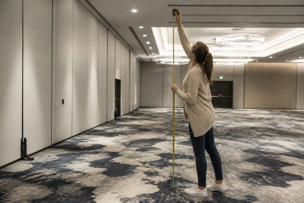 Event coordinator measuring an indoor corporate venue with tape measure, reviewing space dimensions and ceiling height for balloon installation planning