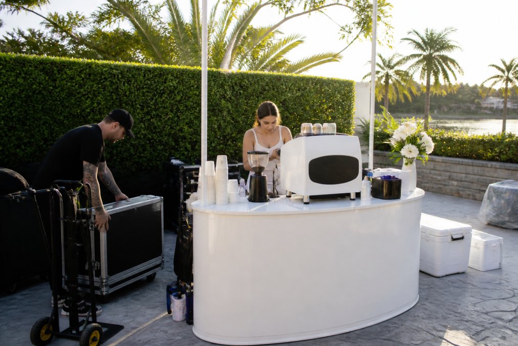 Professional mobile coffee cart set up outdoors at a South Florida event venue with barista preparing specialty drinks for arriving guests, natural afternoon sunlight illuminating the setup