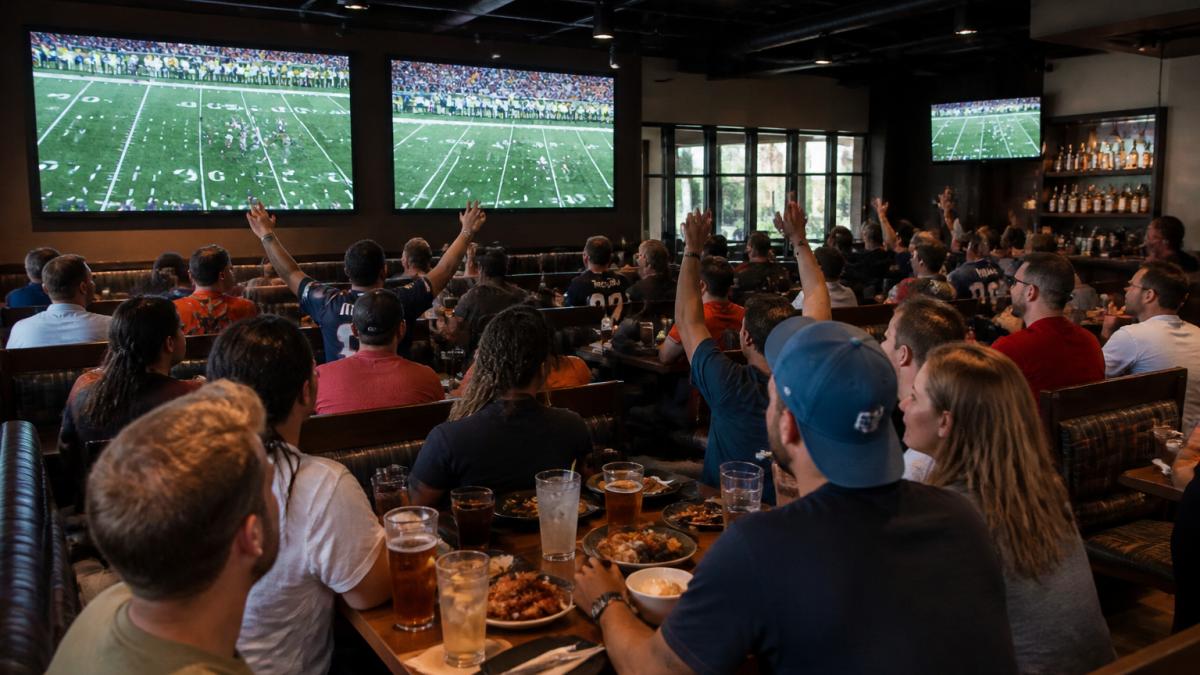 Friends enjoying appetizers and drinks while they plan group watch parties at a sports bar with multiple large screens.