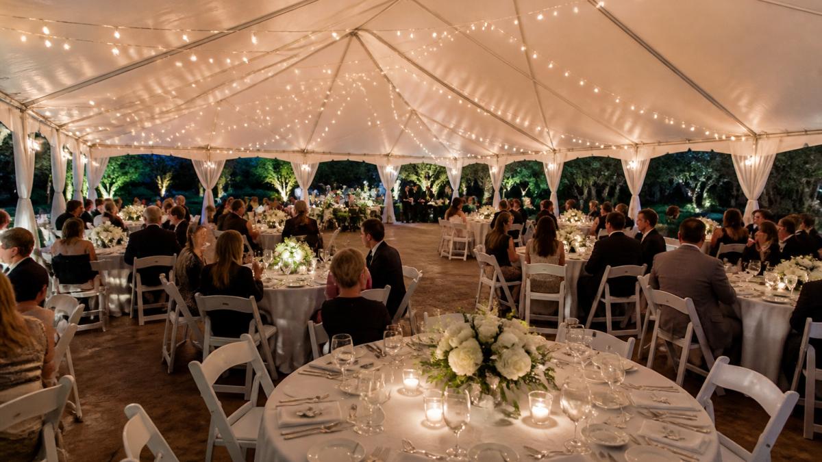 Elegant evening wedding tent rental featuring formal table settings and ambient string lighting for guests