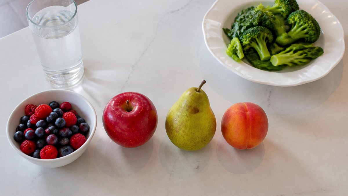 A bowl of berries, apple, pear, and peach representing a phase one fruit serving next to greens and water.
