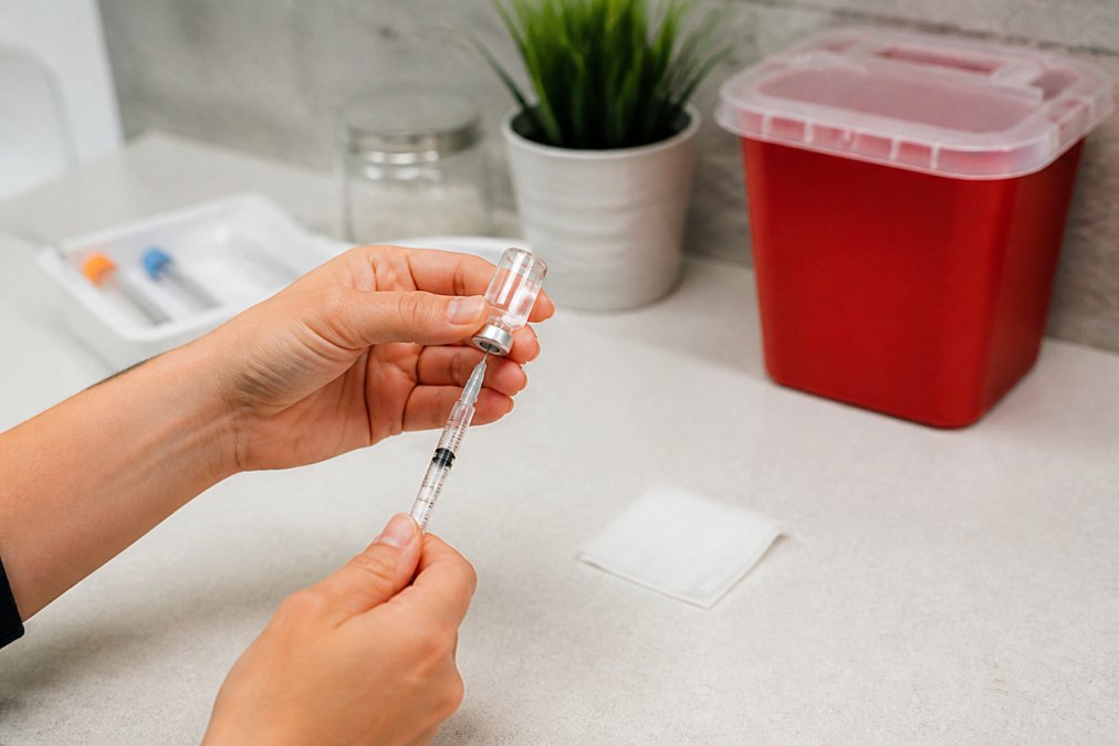 Hands drawing liquid medication for a B12 injection into a syringe from a glass vial on a clean countertop