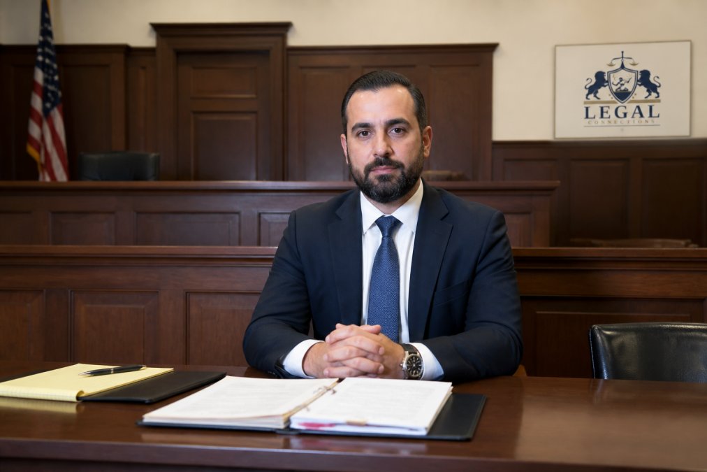 Professional adult in business attire sitting calmly at a table in a courtroom, facing forward with composed expression and organized documents nearby