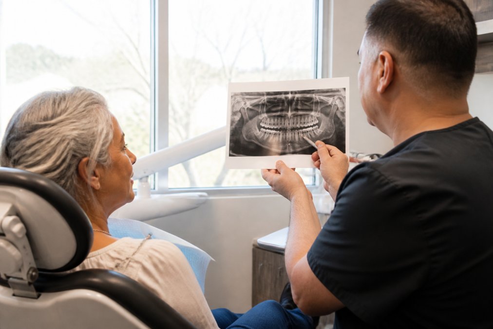 Patient in dental chair during consultation with dentist reviewing 3D imaging results on monitor, natural clinical lighting