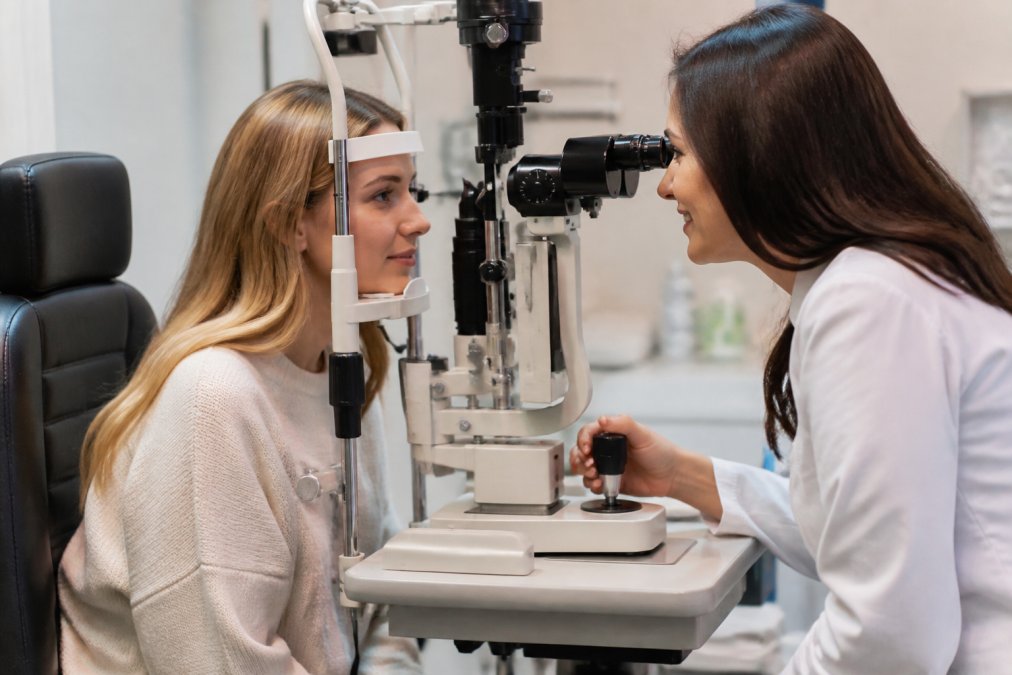 Patient sitting in eye care professional's office during follow-up examination, discussing comfort concerns and adaptation progress with practitioner using slit lamp microscope in modern clinical setting