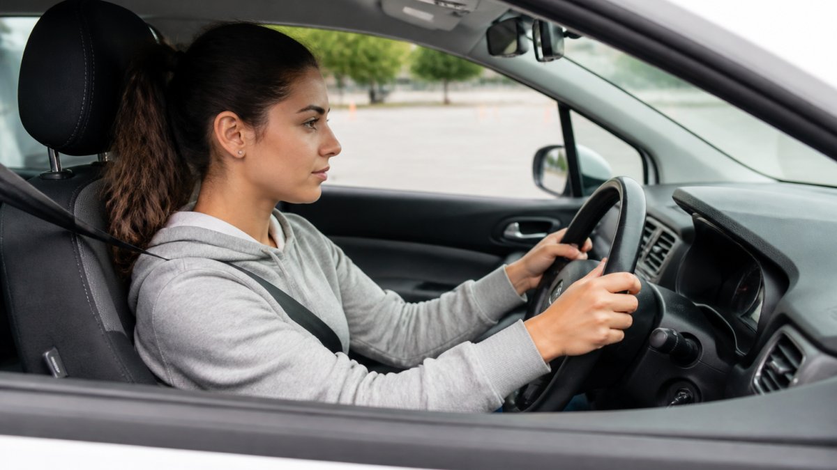 Student adjusting seat and mirrors to prepare first driving lesson with hands at 9 and 3 o'clock positions.