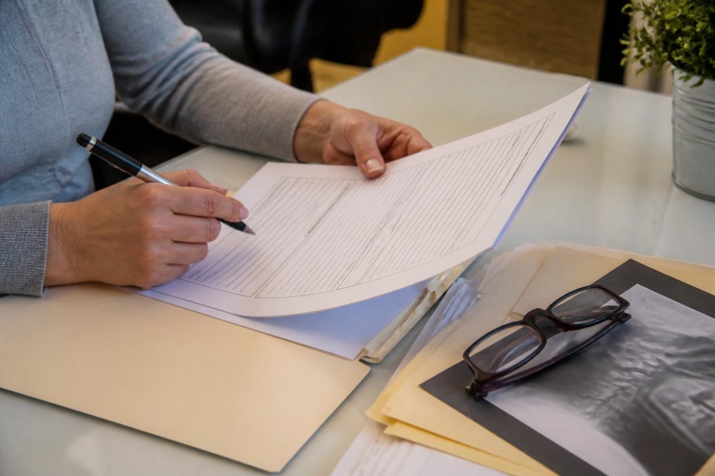 Close-up of hands holding a filled-out health intake form with a pen, medical records, and glasses on a clean desk