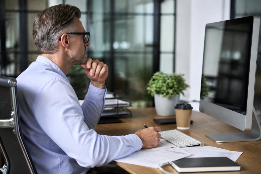 Business owner reviewing financial performance metrics on a computer monitor displaying charts and KPI dashboards in a bright, modern office with organized workspace and professional setting