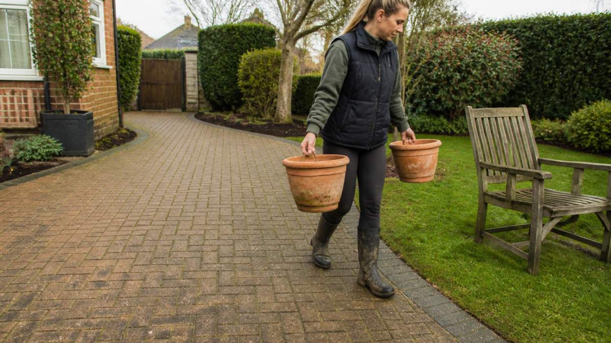 Homeowner moving plant pots and garden chairs off a block paved driveway to ensure it is ready for professional cleaning.