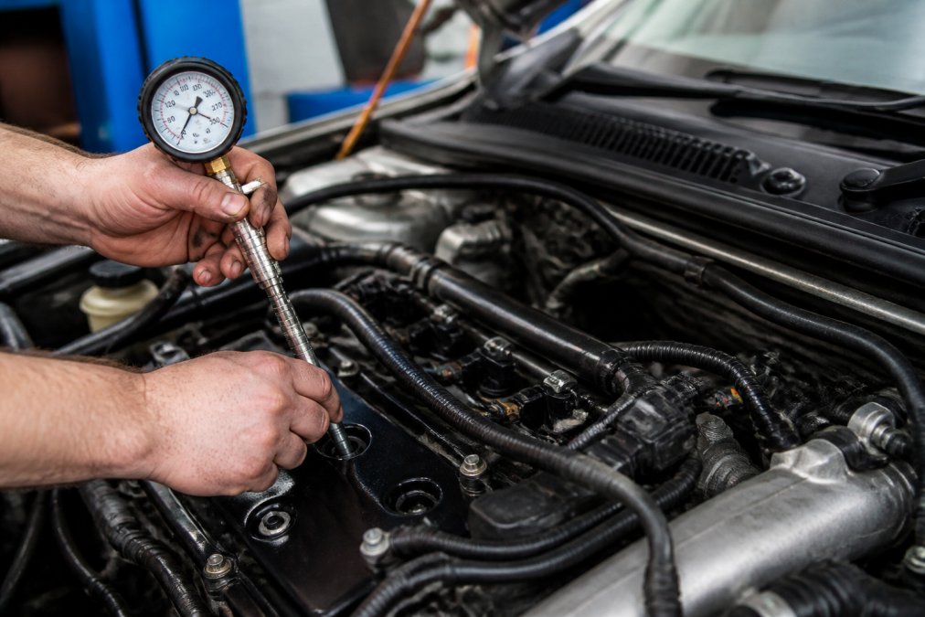 Mechanic attaching a compression gauge to test engine health before supercharger installation.