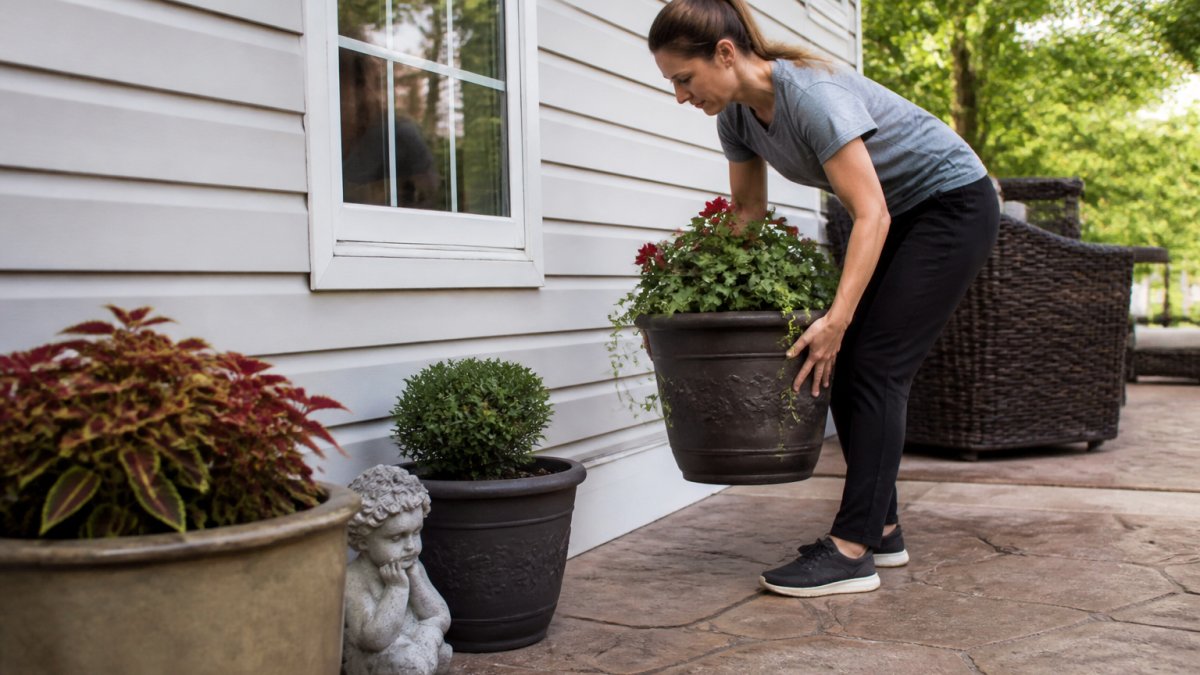 Homeowner moving outdoor furniture, potted plants, and decorations away from the side of a house before pressure washing begins