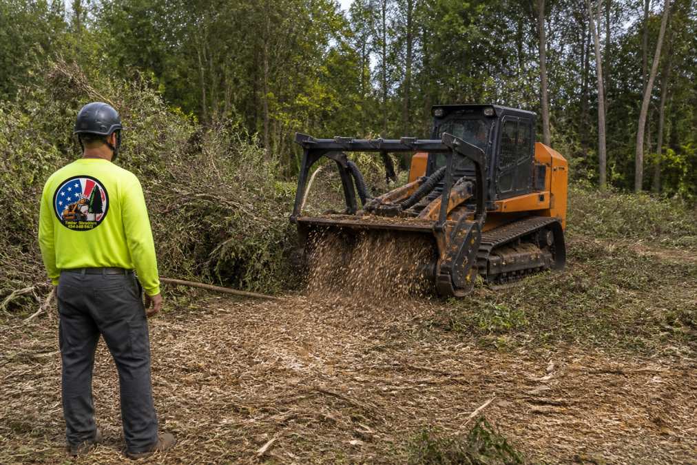 Heavy forestry mulching equipment clearing dense brush and vegetation from a rural property, grinding overgrown trees and brush into mulch while operators manage the equipment on the cleared land