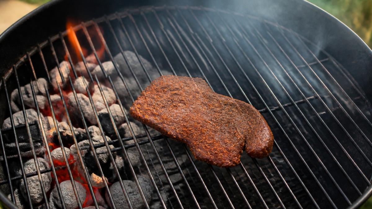 Meat arranged on a grill grate away from direct flames with charcoal set to one side to create an indirect heat zone