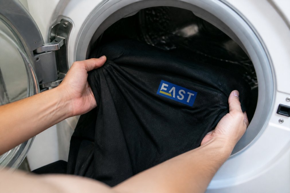 Close-up of a work shirt being turned inside out before washing, showing the logo on the reverse side inside a washing machine drum with cold water