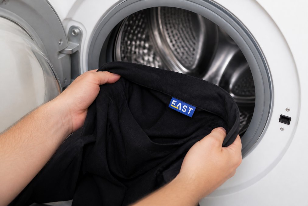 Close-up of work uniforms being turned inside out before washing, showing the printed logo facing inward as the garment enters a washing machine drum