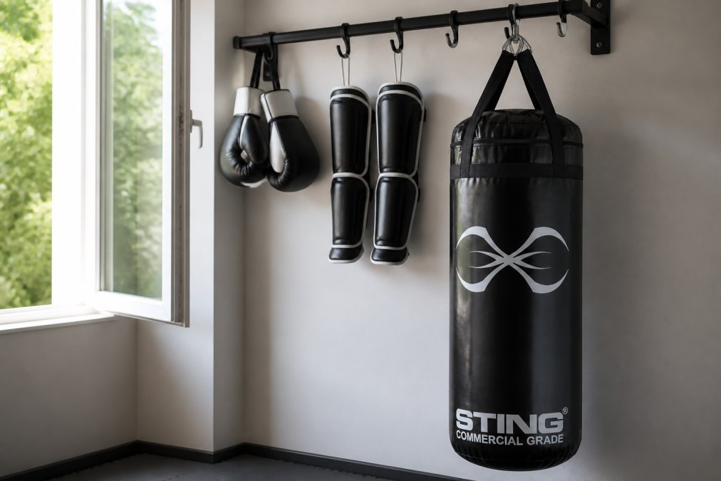 Boxing gloves and shin guards hanging on a wall-mounted rack near an open window with natural light, showing proper air circulation setup in a clean home gym space
