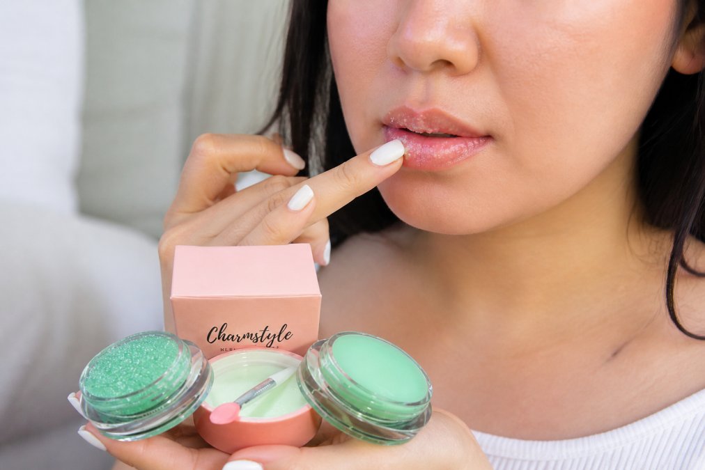 Close-up of hands gently applying a moisturizing lip scrub with circular motions on lips, showing the soft texture and hydrating formula being worked into the lip surface