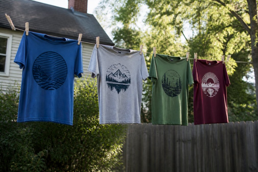 Screen-printed shirts hanging on a clothesline outdoors to air dry, with clear sunlight and a residential background