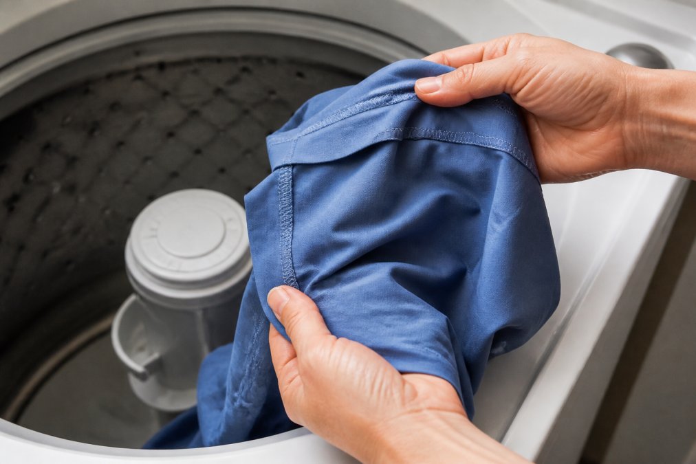 Close-up of hands turning medical scrubs inside out over a washing machine, showing the reverse side of the fabric clearly with the interior seams and stitching visible