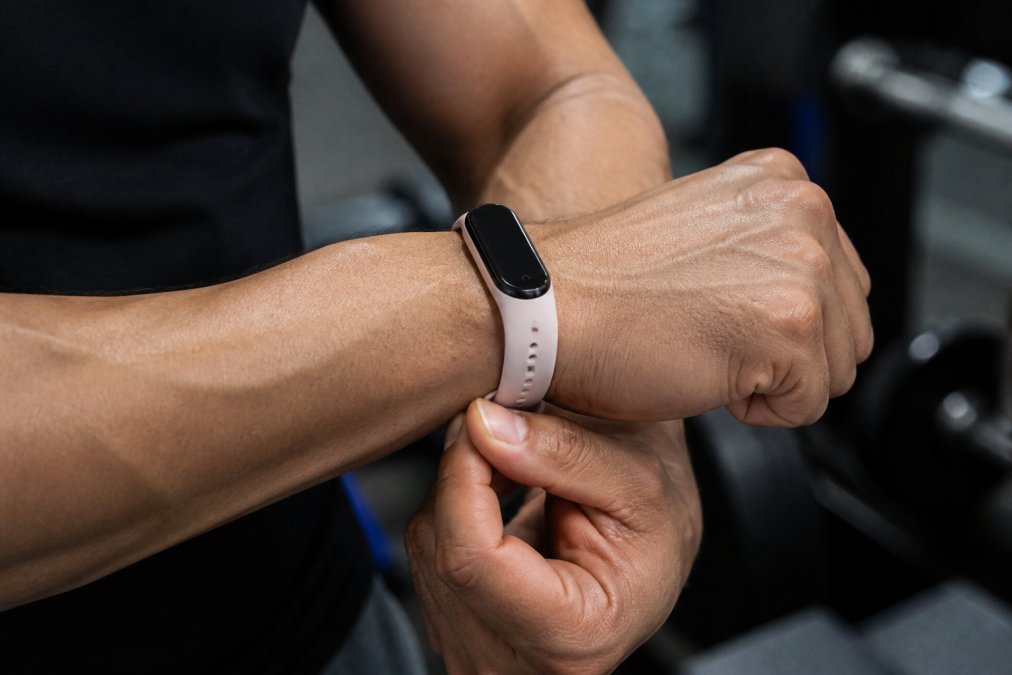 Close-up of hands adjusting and securing a silicone wrist band strap on a muscular wrist, showing proper positioning above the wrist bone during tightening