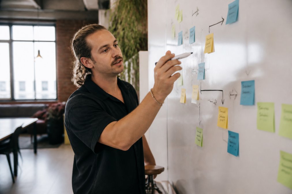 A consultant in a modern Australian office writing on a whiteboard, mapping out a service package structure with sticky notes and markers