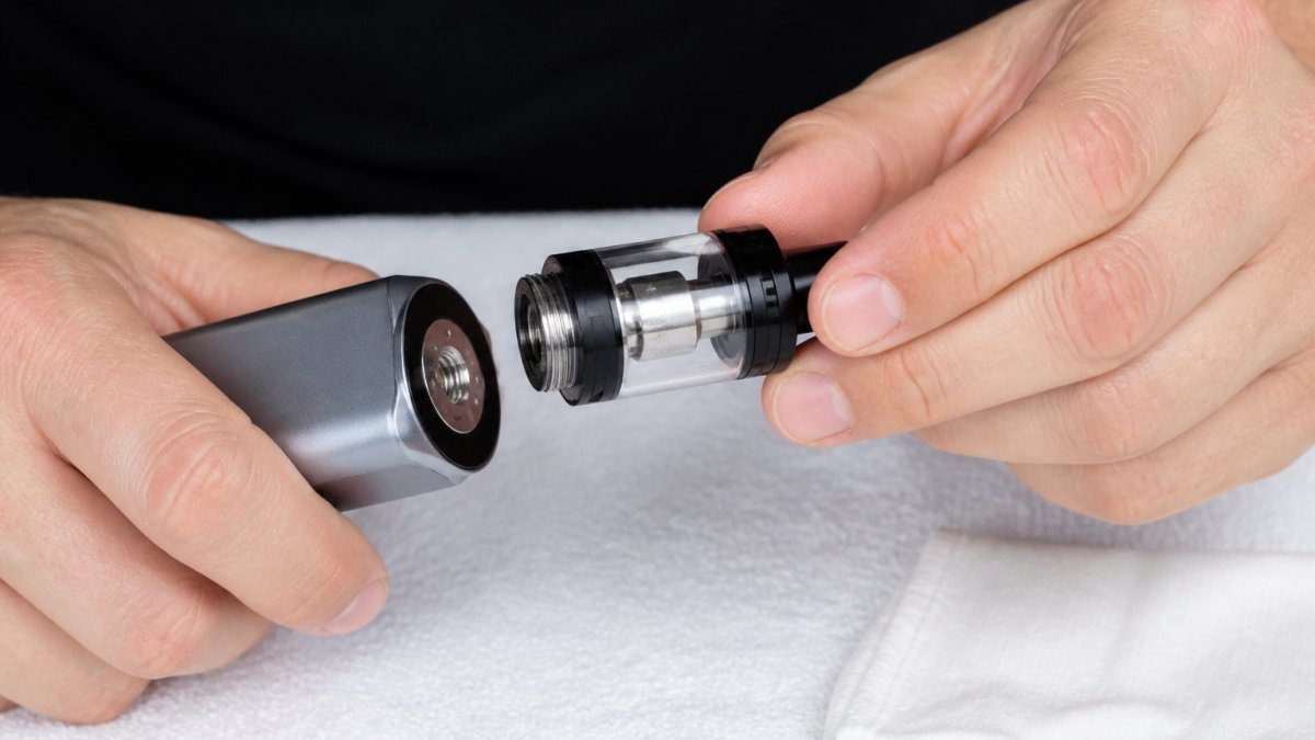Close-up of hands carefully unscrewing a vape tank from a vape mod over a clean white cloth, showing the threading connection and the separation of components