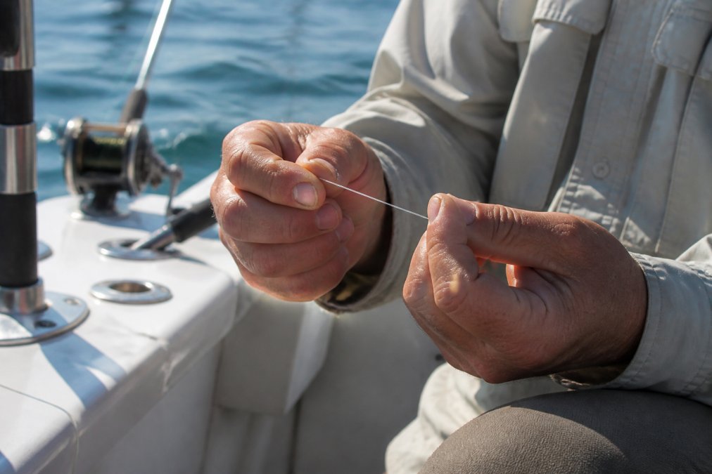 Angler checking monofilament leaders for damage with fingers on a boat deck